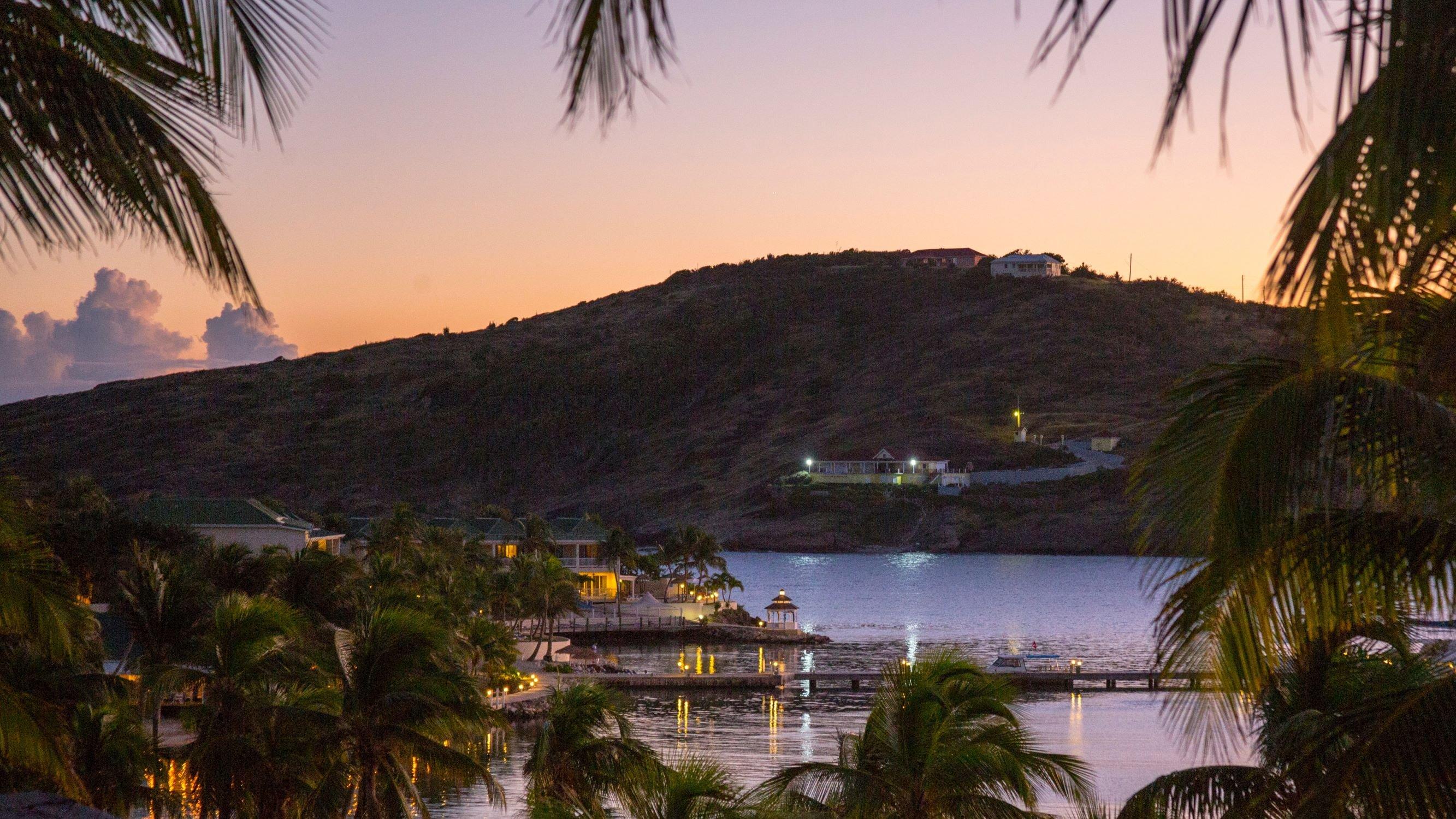 Bucht vor Antigua im Sonnenuntergang mit Blick auf romantisch beleuchtete Hafenstädte, Palmen und das Meer 