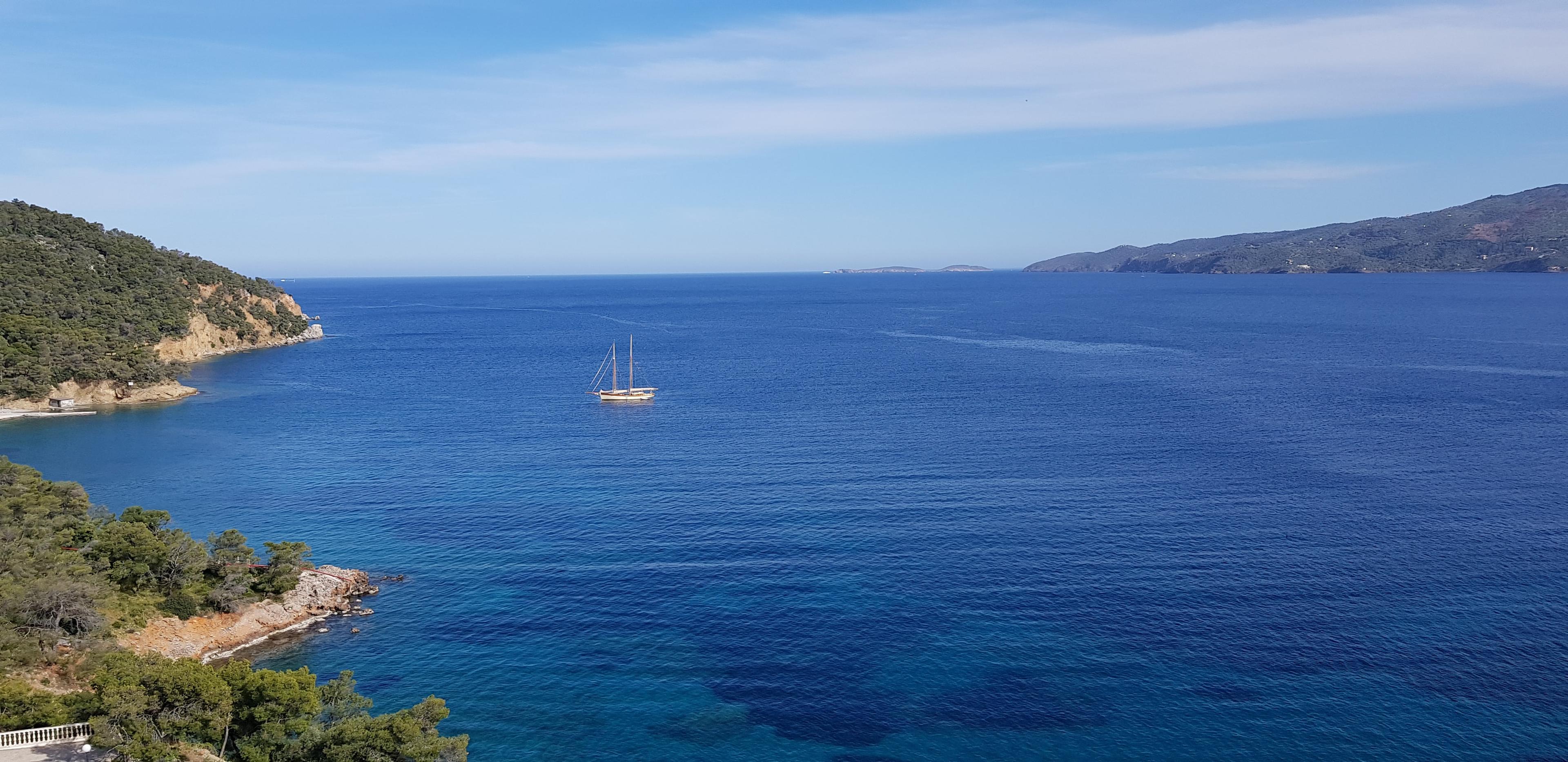 Blick auf felsige Küsten vor Poros, umgeben vom blauen Meer und einem Segelboot