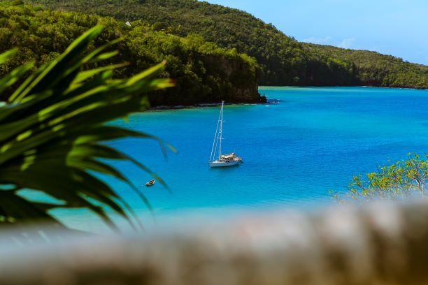 Yacht im glasklaren, blauen Meer vor Antigua umgeben von grün bewachsenen Buchten