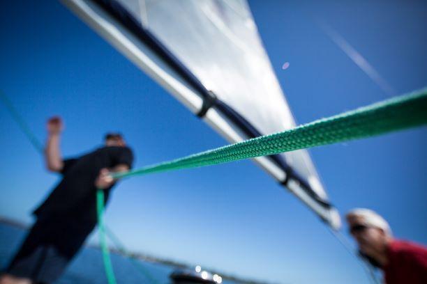 Blick von der Segelyacht auf das Segel, ein Seil und die Crew auf dem offenen Meer bei sonnigem Wetter 