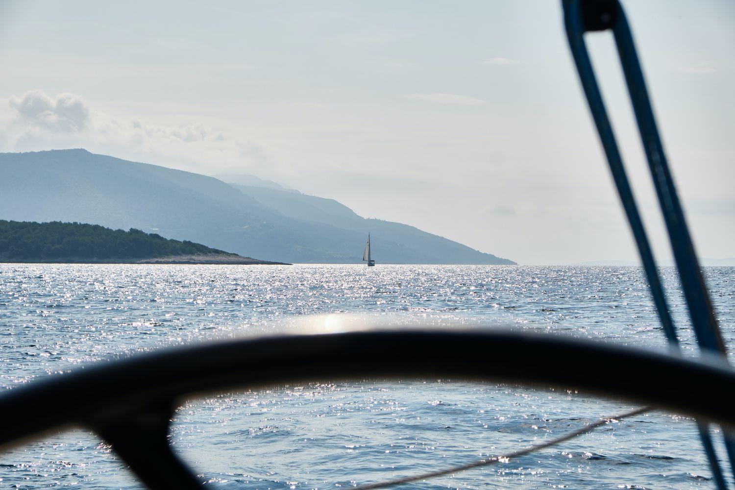 Blick über das Steuerrad einer Segelyacht auf das weite Meer vor Nordkroatien bei sonnigem Wetter und ruhiger See